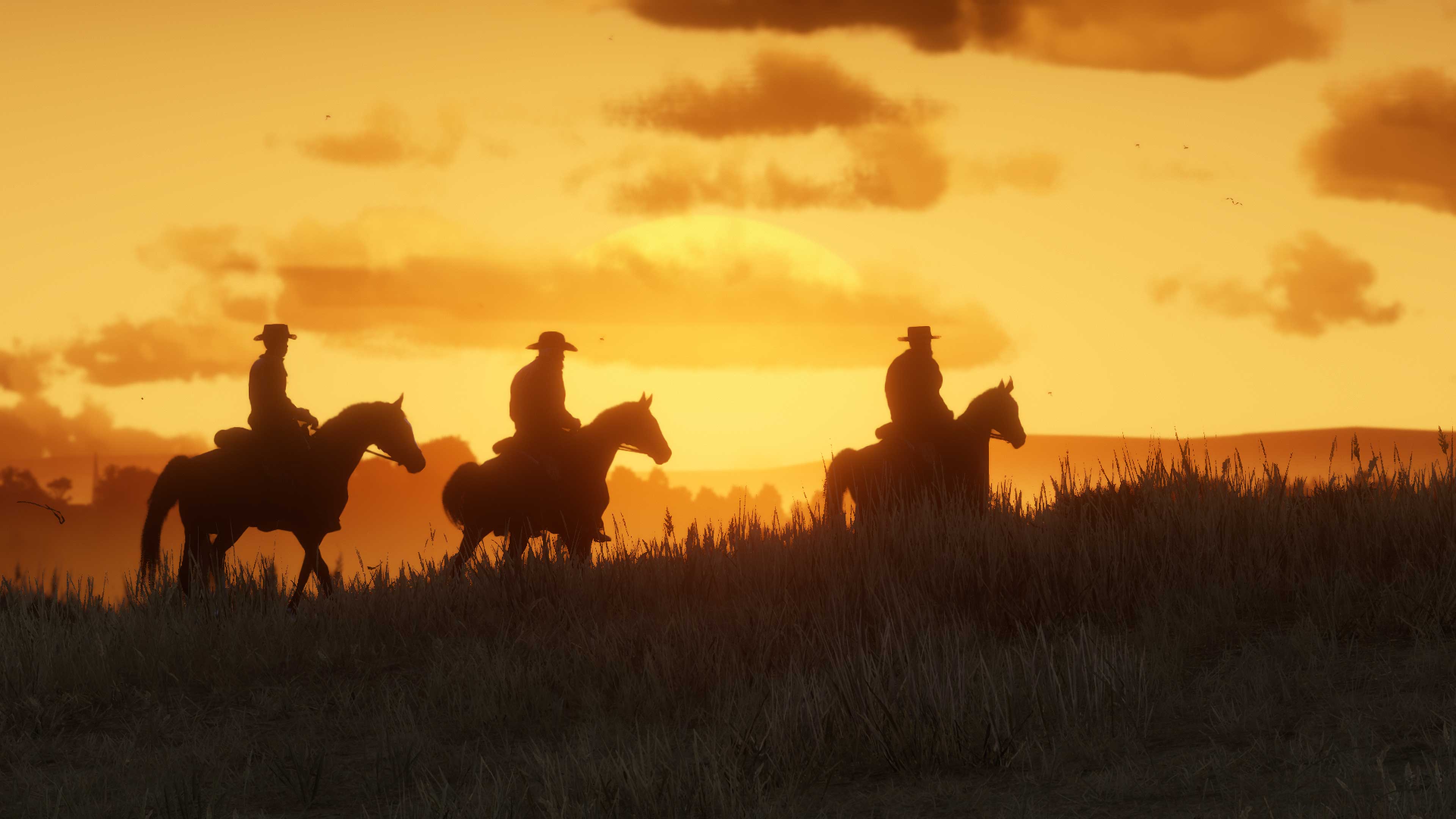 Sagome di tre personaggi di Red Dead Online a cavallo che vagano lungo una collinaon un cielo dorato sullo sfondo.