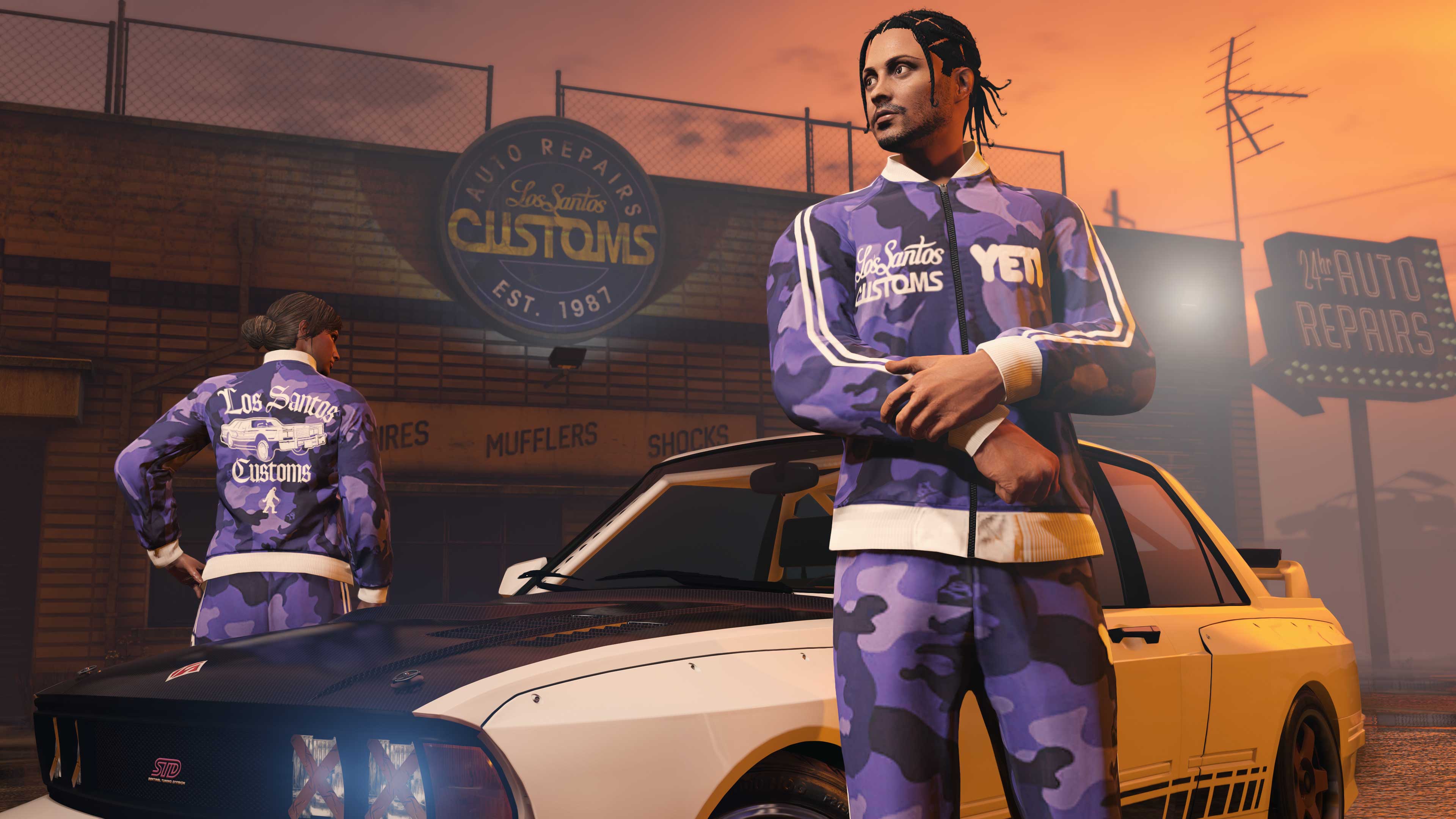 Two GTA Online character wear the Yeti x LS Customs Tracksuit near a car outside the Los Santos Customs building.